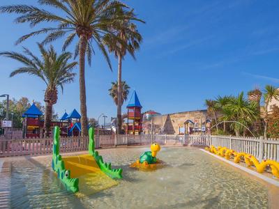 Parc aquatique pour enfants avec fontaines vertes et jaunes près des palmiers et d'une aire de jeux.