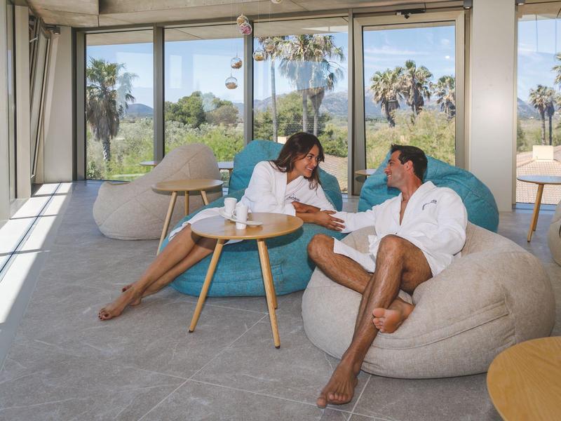 Un couple se détend sur des poufs dans une pièce lumineuse avec de grandes fenêtres donnant sur un paysage.