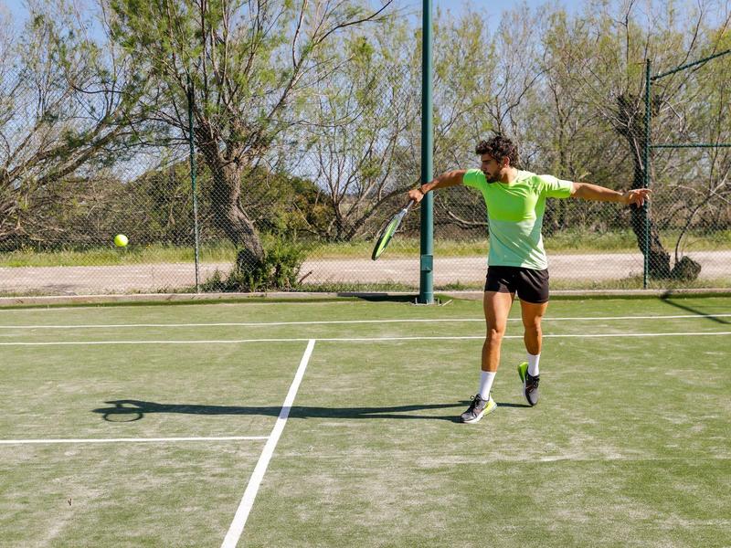 Homme jouant au tennis sur un terrain extérieur par temps ensoleillé.