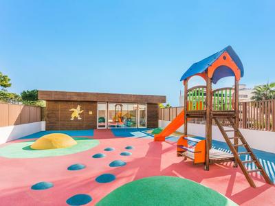 Parco giochi colorato per bambini con scivolo e struttura da arrampicata sotto un cielo sereno nel giardino dell'hotel.