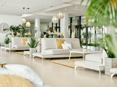 Area lounge luminosa e moderna con divani bianchi, piante verdi e luce naturale.