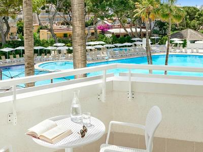 Balcone con tavolo e sedia che si affacciano su una piscina e palme in un resort.