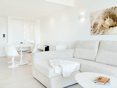 Soggiorno luminoso con divano bianco, tavolo da pranzo con sedie e decorazione murale moderna.