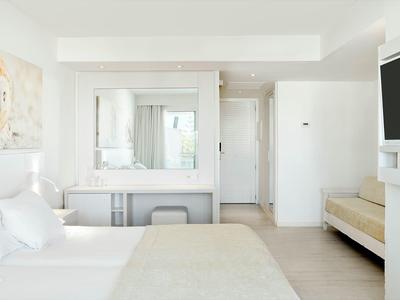 Camera d'albergo luminosa con letto grande, specchio, TV e arredamento chiaro.