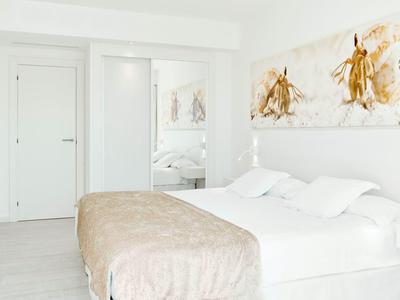 Camera luminosa con letto matrimoniale, pareti bianche e opera d'arte dorata.