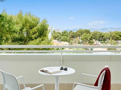 Balcone con piccolo tavolo bianco e due sedie con vista su alberi verdi e cielo azzurro.
