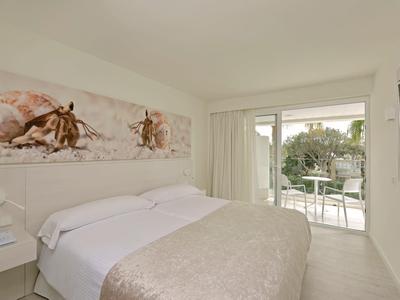 Chambre lumineuse avec lit double, œuvre d'art au-dessus de la tête de lit et balcon avec vue sur le jardin.