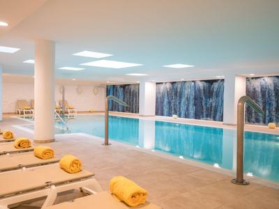 Piscine intérieure avec chaises longues et serviettes jaunes dans un espace bien-être lumineux.