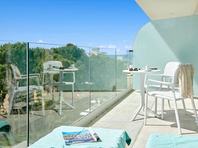 Balcon lumineux avec chaises blanches et garde-corps en verre donnant sur des arbres verts.