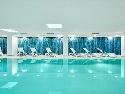 Piscine intérieure moderne avec murs d'eau bleus et chaises longues blanches.