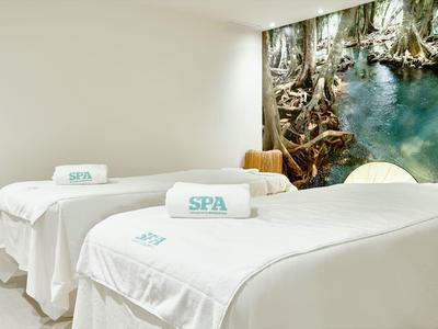 Deux tables de massage spa avec serviettes blanches dans une pièce claire avec une fresque murale nature.