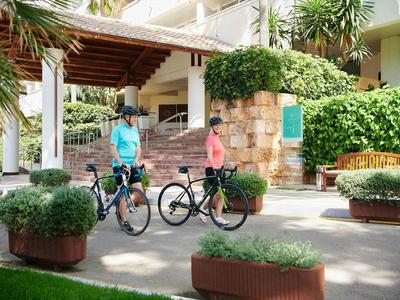 Deux personnes avec des vélos devant un hôtel avec une végétation luxuriante et des marches.