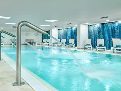 Moderní vnitřní bazén s vodními tryskami a lehátky v světlé wellness oblasti