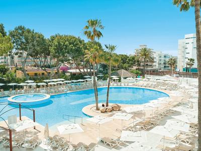 Gran piscina exterior con palmeras, tumbonas y sombrillas bajo cielo azul