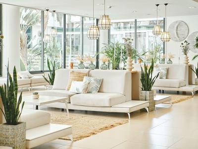Sala de hotel moderna y luminosa con sofás blancos, plantas y grandes ventanas con vista al exterior.