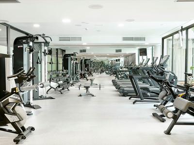 Salle de sport lumineuse avec équipements modernes et grandes fenêtres laissant entrer la lumière naturelle.