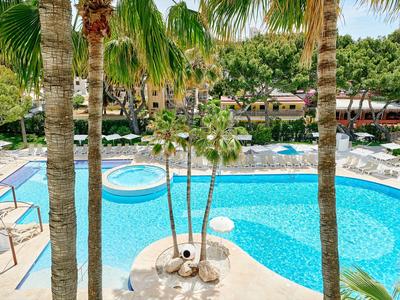 Piscine d'hôtel avec palmiers, chaises longues et environnement verdoyant par une journée ensoleillée.