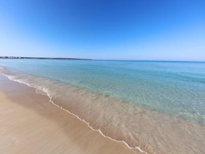Klares, ruhiges Meer trifft auf sanfte Sandküste unter strahlend blauem Himmel.