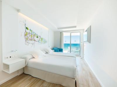 Helles Schlafzimmer mit zwei Betten, großem Fenster und Blick auf das blaue Meer.