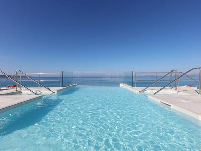 Piscina a sfioro con vista sul mare sotto un cielo terso e azzurro.