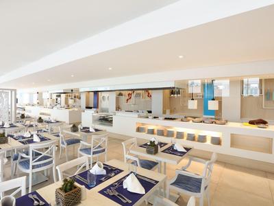 Světla, moderní restaurace s bílým nábytkem a modře prostřenými stoly.