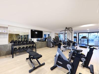 Palestra luminosa con attrezzature moderne, pesi e grandi finestre in hotel.