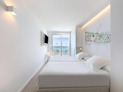 Hell eingerichtetes Schlafzimmer mit großem Bett, Wandbild und Blick auf Balkon und Meer.