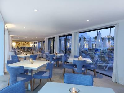 Modernes Restaurant mit blauen Stühlen, weißen Tischen, großen Fenstern und hellem Deckenlicht.