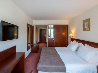 Helles Hotelzimmer mit großem Bett, Wandfernseher und warmem Holzmobiliar.