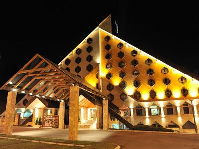 Beleuchtetes Hotelgebäude bei Nacht mit Pyramidendach und Eingangsbereich aus Holz und Stein