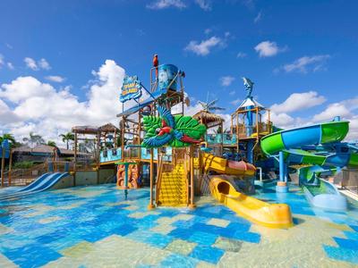 Wasserpark mit bunten Rutschen, Spielgeräten und flachem Becken unter blauem Himmel.