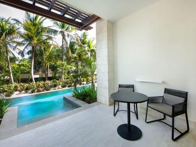 Moderner Außenbereich mit kleinem Pool, weißen Wänden, zwei Stühlen und rundem Tisch unter Dach.