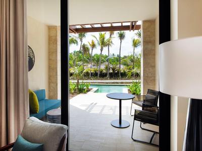 Helles Zimmer mit Stühlen, Tisch und Blick auf Pool und Palmen durch große Glasschiebetür.