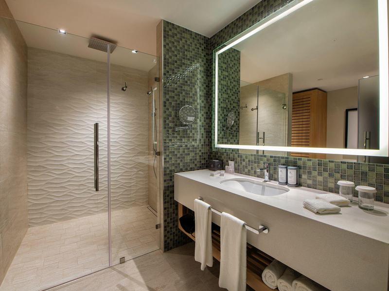 Modernes Badezimmer mit begehbarer Dusche, großer Spiegelwand und hellen Mosaikfliesen an der Wand.