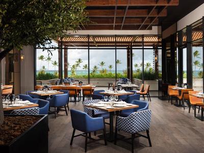 Modernes Restaurant mit blauen Sesseln, Holzdecke und großen Fenstern mit Blick ins Grüne.