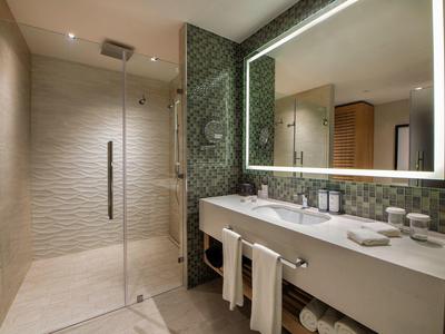 Modernes Badezimmer mit begehbarer Dusche, großer Spiegelwand und hellen Mosaikfliesen an der Wand.