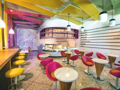 Moderne Café mit runden Tischen, pinken Stühlen, gelben Barhockern und bunten Deckenlampen.