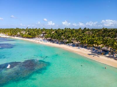 Acqua turchese e spiaggia di sabbia bianca con palme e lettini in una località tropicale.