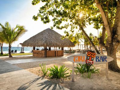 Bar sulla spiaggia con tetto di paglia, palme e luce solare, vista sul mare al tramonto.