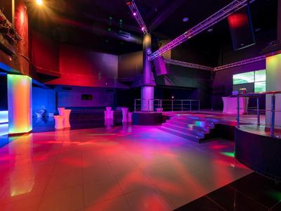 Leerer Nachtclub mit Bühne, bunten Lichtern und Tanzfläche in warmen Rot- und Blautönen.