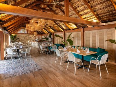 Hell beleuchteter Speisesaal mit Holzdach, weißen Stühlen und Tischen, dekoriert mit Pflanzen.