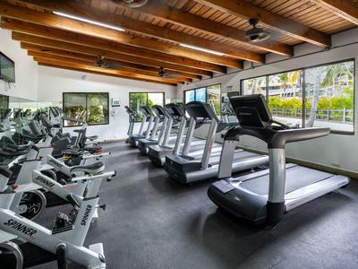 Helles Fitnessstudio mit Holzbalkendecke, Laufbändern und Ergometern entlang der Fenster.