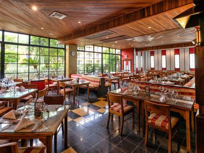 Modernes Restaurant mit Holztischen, Stühlen und großen Fenstern, viel Tageslicht und dekorativer Decke.