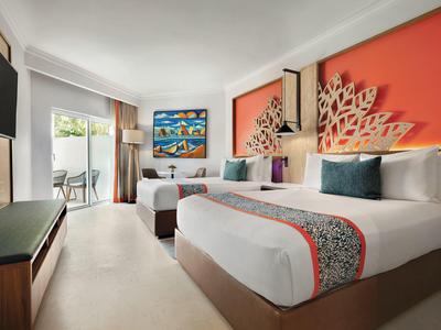 Hotelzimmer mit zwei großen Betten, buntem Wandbild und Zugang zum Balkon mit grünem Ausblick.