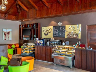 Gemütliches Café mit bunten Stühlen, Holzdecke und Tresen mit Kuchen und Kaffeemaschine.