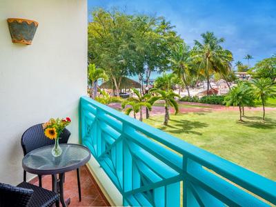 Balkon mit blauem Geländer, Tisch mit Sonnenblumen, Blick auf grüne Bäume und blauen Himmel.