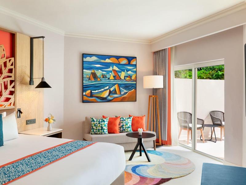 Helles Schlafzimmer mit großem Bett, buntem Wandbild, Sofa, Teppich und Zugang zu Terrasse.