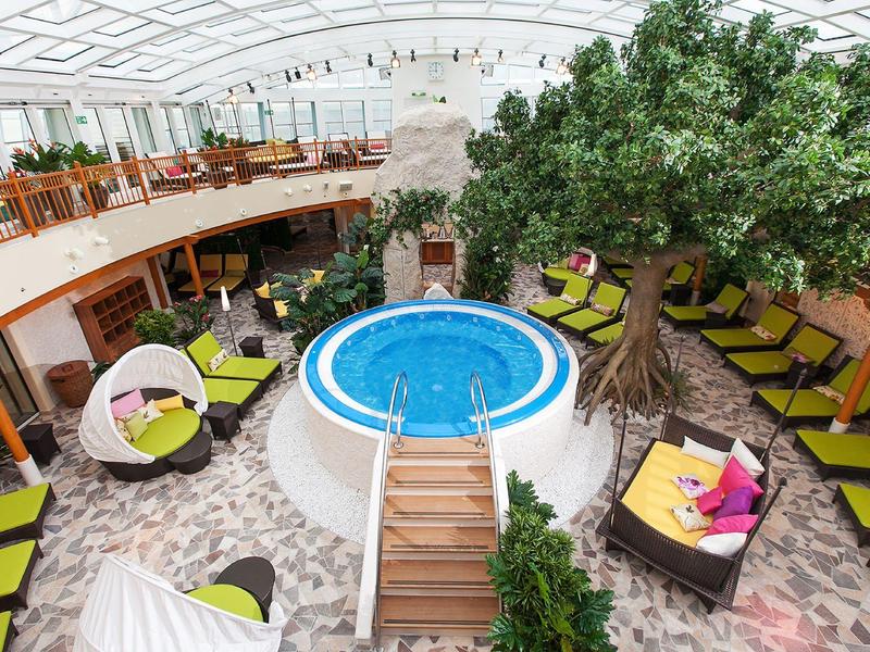 Innenraum mit kleinem Pool, großen künstlichen Baum, bunten Sitzmöbeln und gemütlichen Liegen.