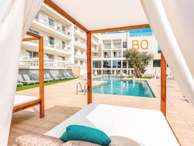 View from a daybed towards a pool and a multi-story hotel building.