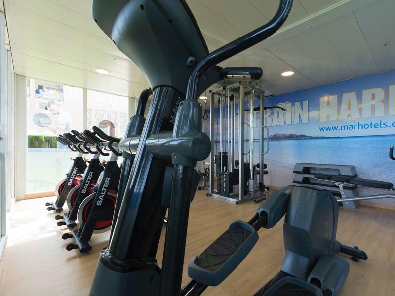 Moderne Fitnessgeräte in einem hellem, gut ausgestatteten Fitnessraum mit großen Fenstern.